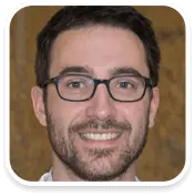 Smiling man with short dark hair, wearing rectangular black glasses and a beard, looking directly at the camera.